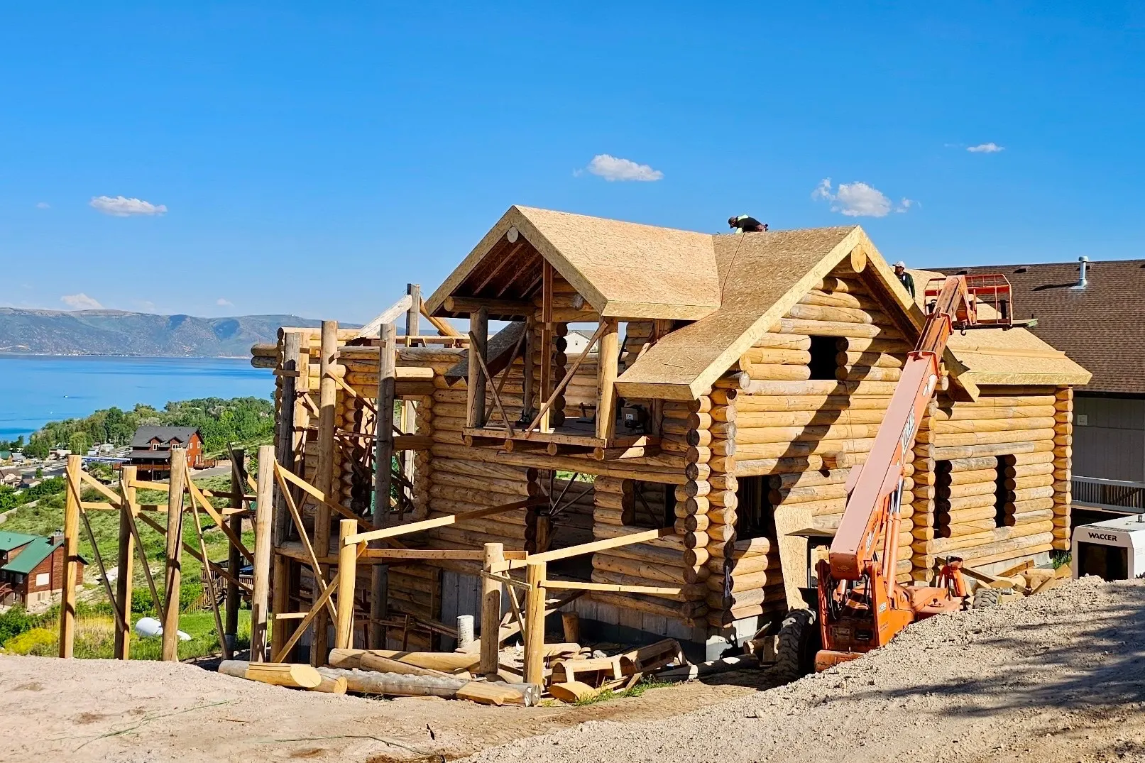 Round-log home under construction with workers and equipment on site